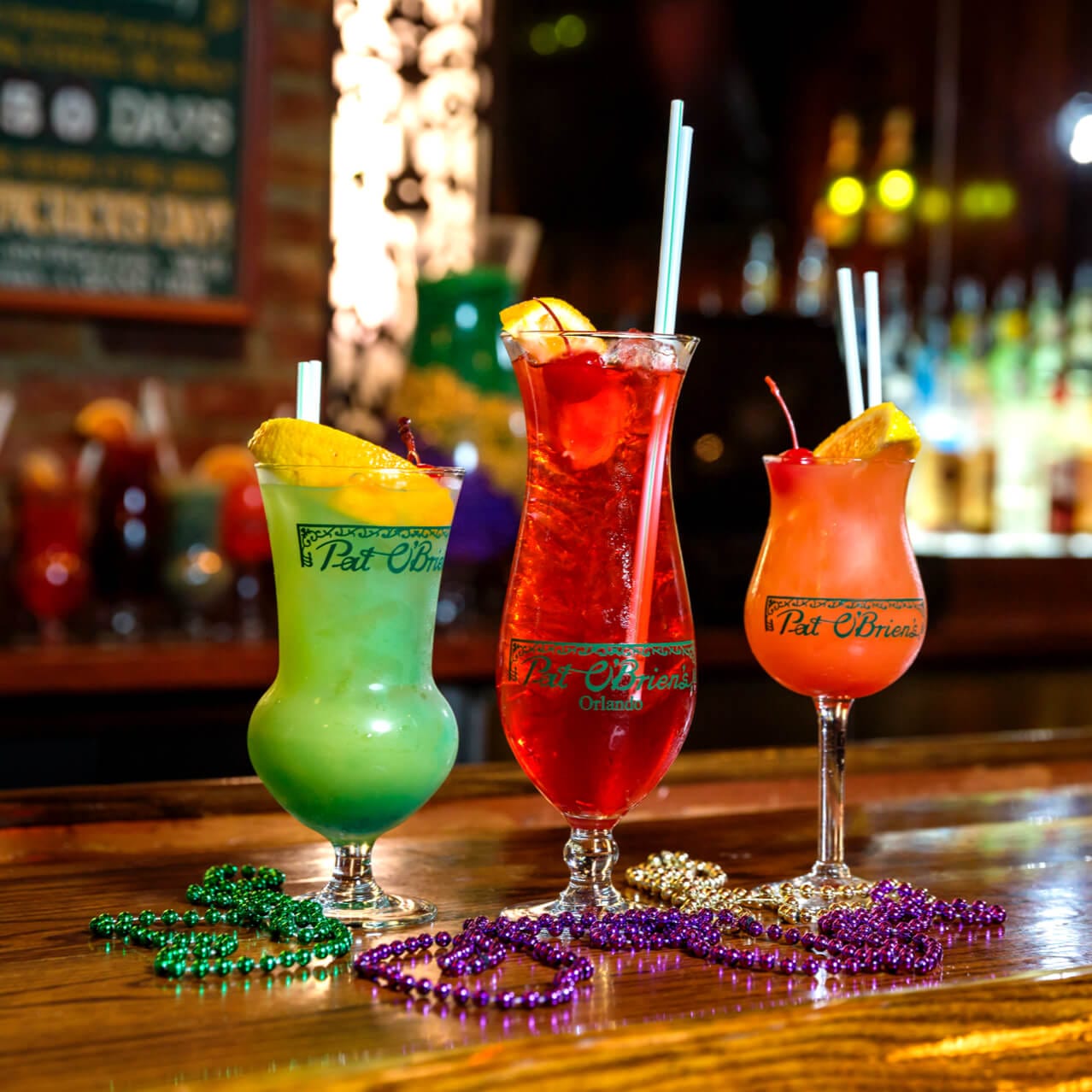 Boldly colored green, red, and orange cocktails with Mardi Gras beads on the bar top inside Universal CityWalk's Pat O'Brien's.