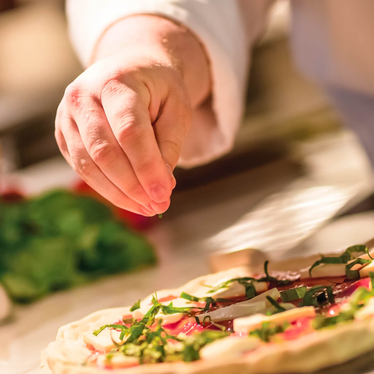 A chef sprinkles chopped basil on a fresh pizza at Universal CityWalk's Red Oven Pizza Bakery.