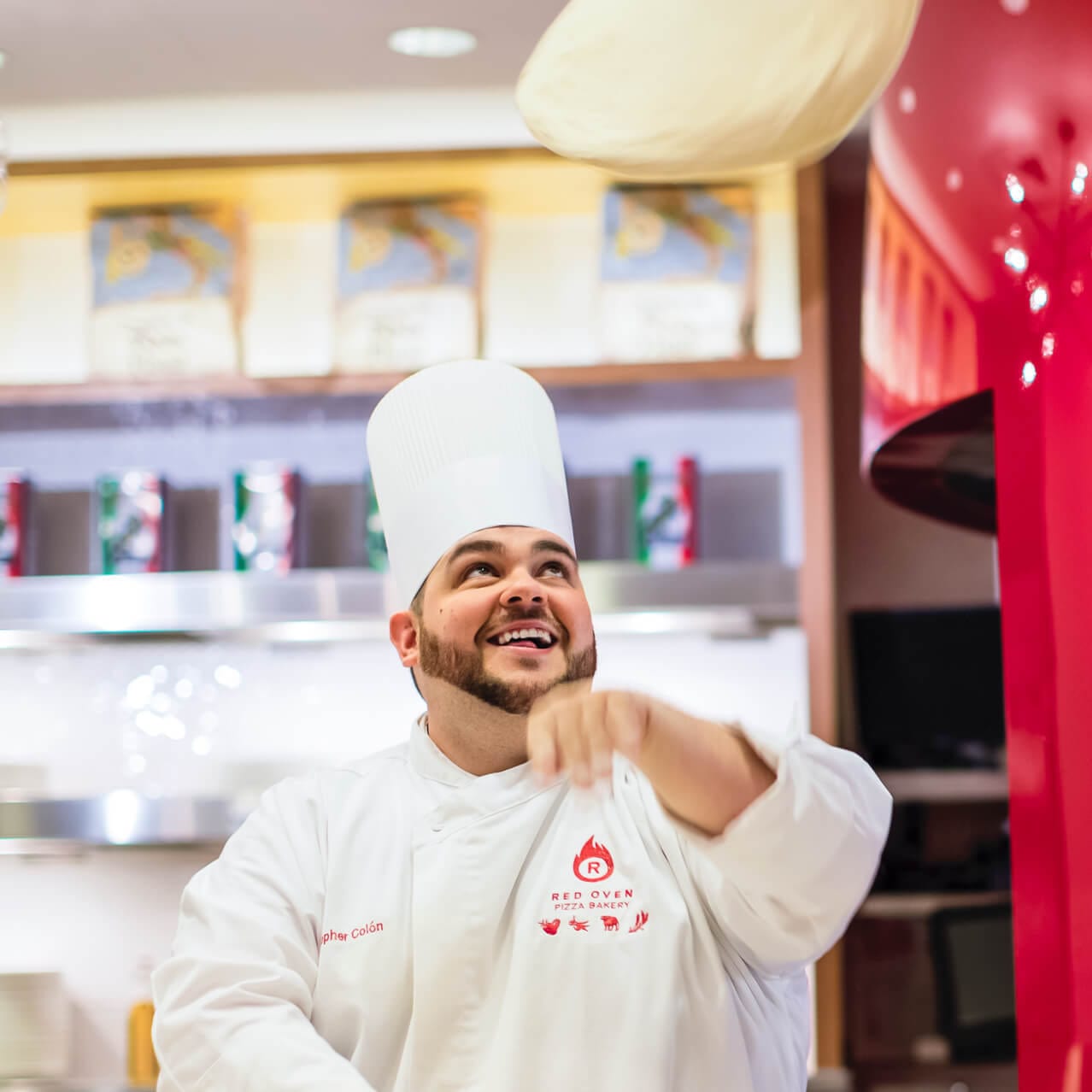 A chef at Red Oven Pizza Bakery tosses dough in the air as he crafts a made to order pizza.