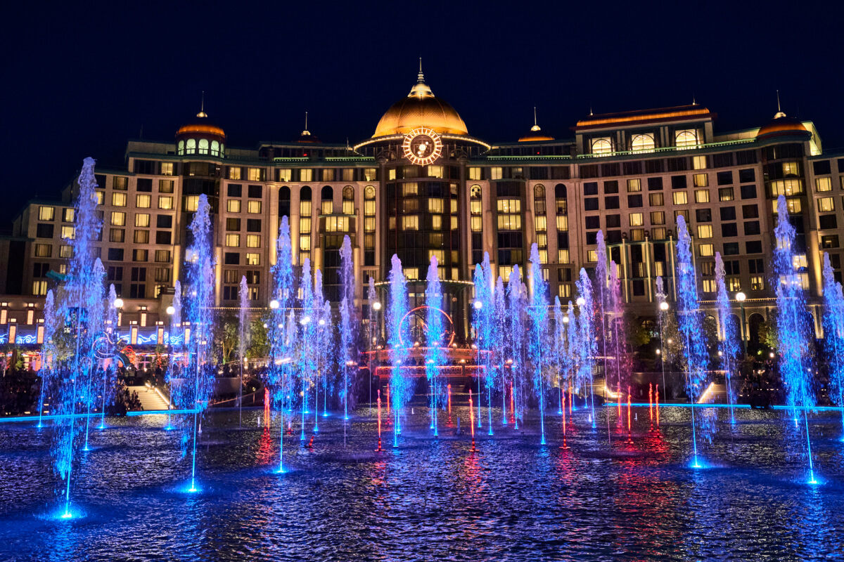 The illuminated fountain at night in front of the Universal Helios Grand Hotel at Universal Epic Universe.