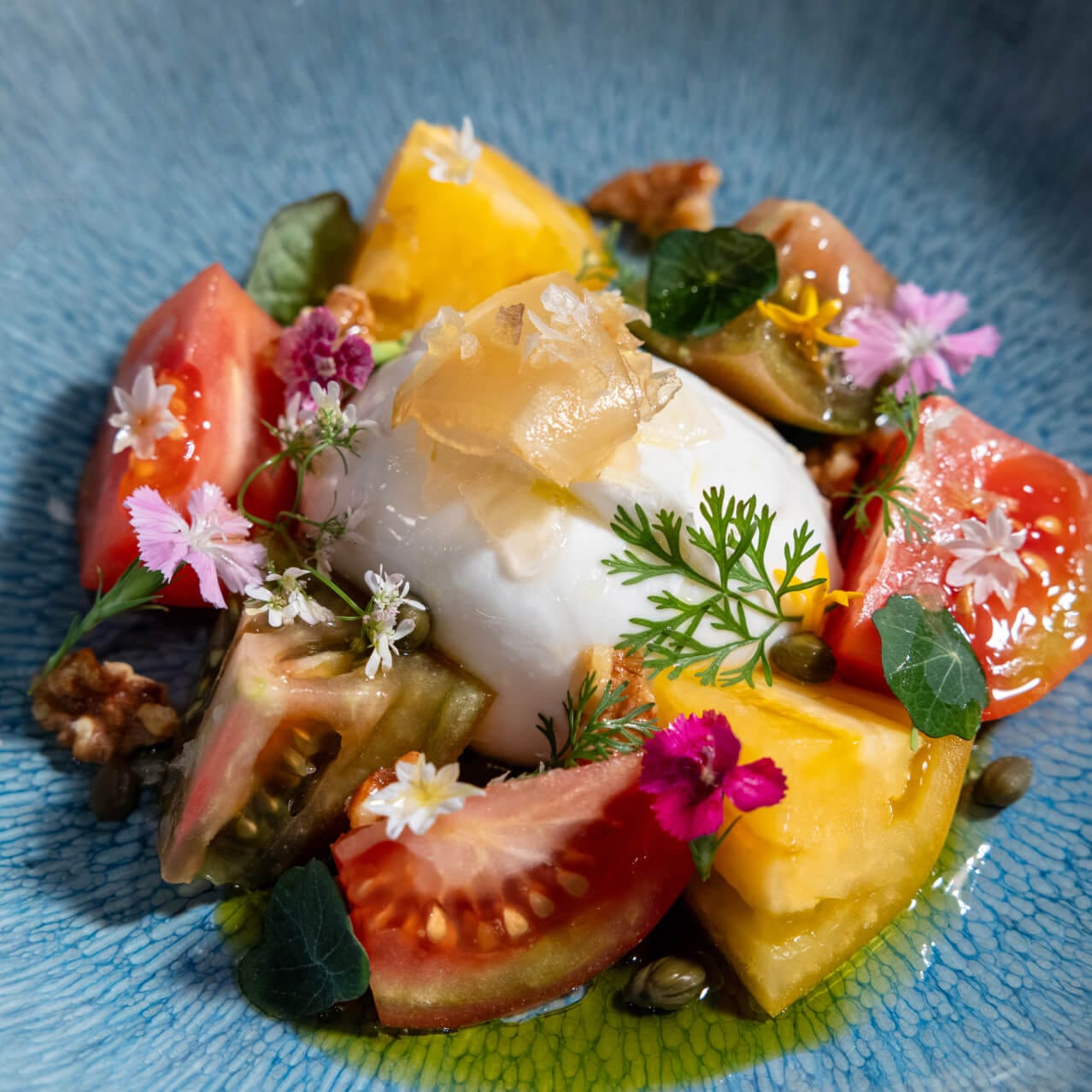Heritage Tomato & Burrata Salad with mostarda, capers, agave walnuts, Reggiano pesto and microgreens, served at Flora Taverna.