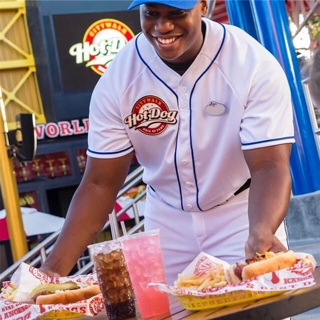 A waiter in a white baseball uniform serves hot dogs to two guests at Universal CityWalk.