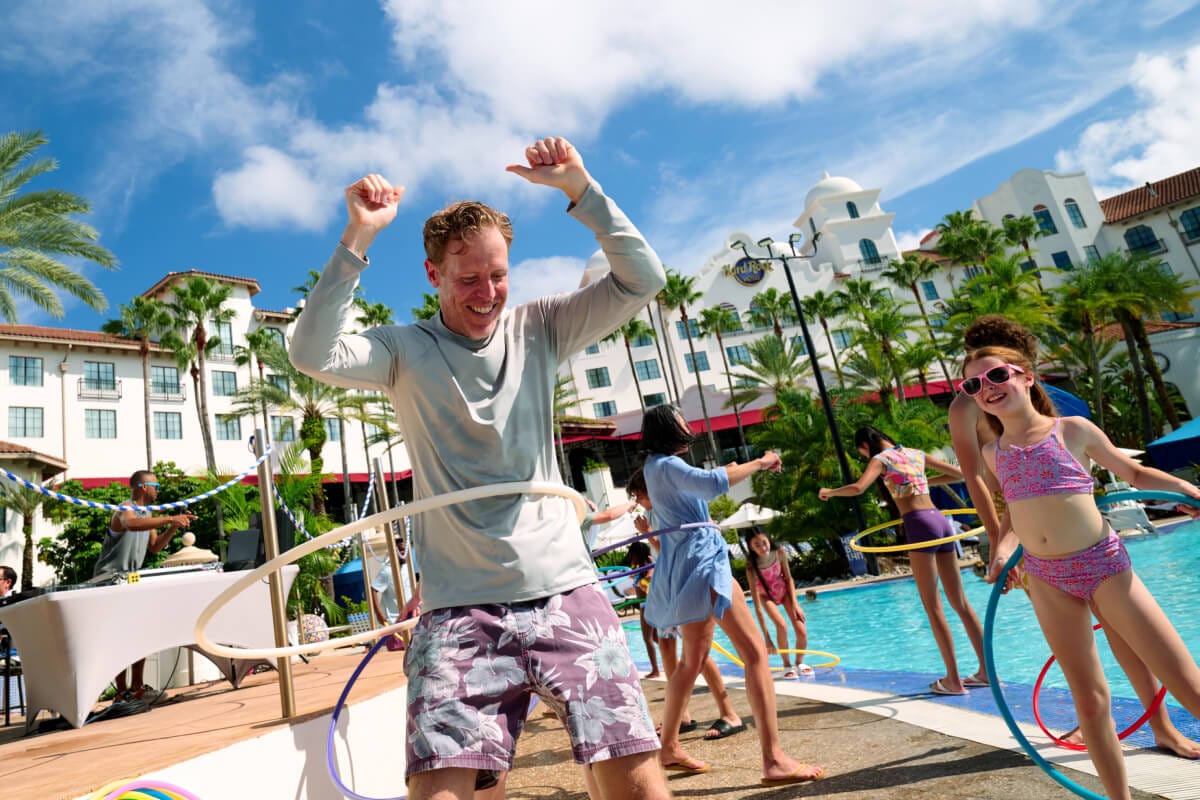 An excited family hula-hooping with other Guests on the deck of a pool with the Hard Rock Hotel in the background.