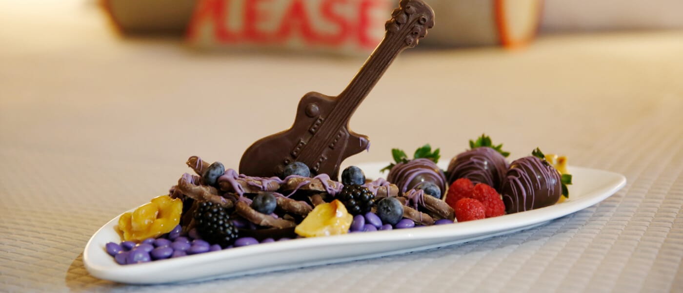 A room service provided tray of chocolate covered strawberries, candies, fruit, and a chocolate guitar on display inside a guest room at Hard Rock Hotel in Universal Orlando.