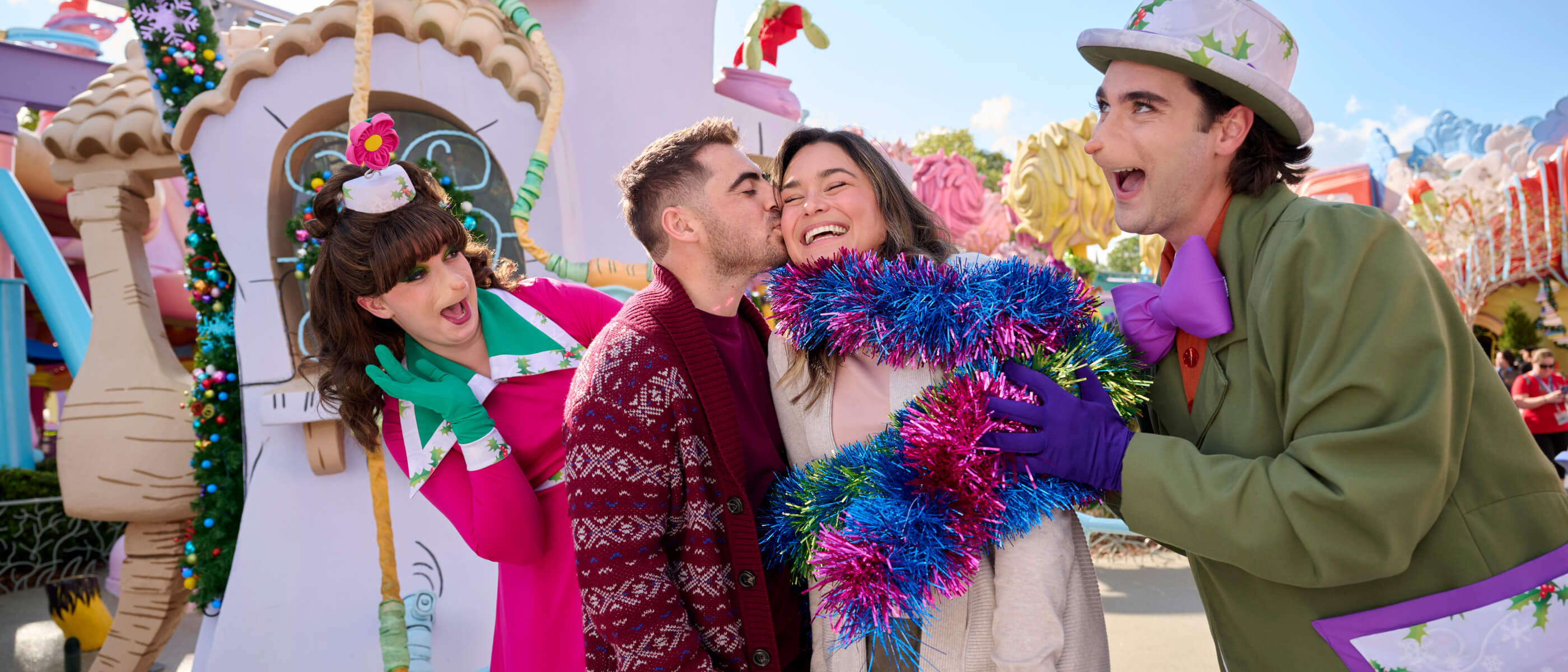 One Guest kissing the cheek of another wrapped in garland as two Whos smile gleefully in colorful Who-ville.