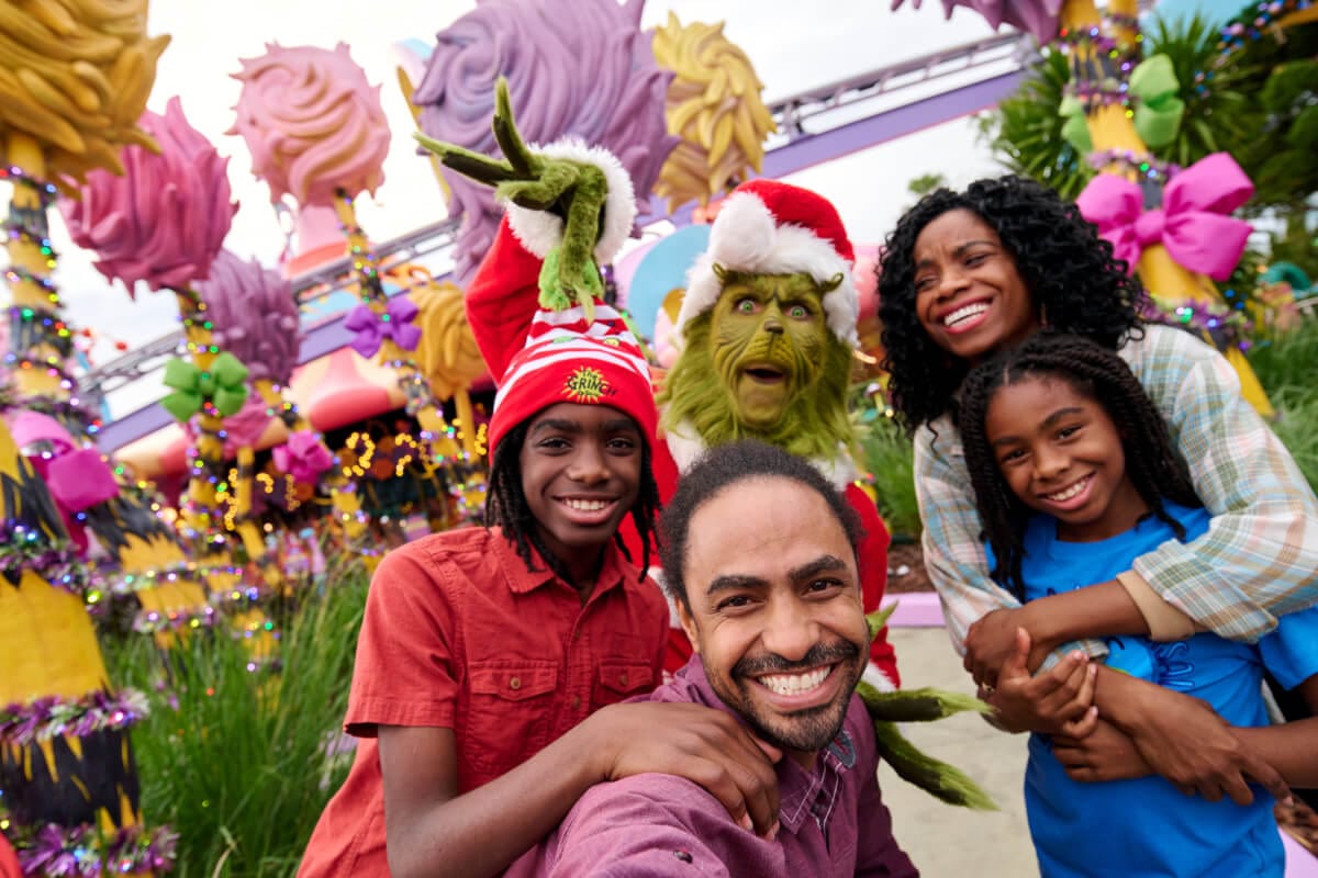 Selfie of a family smiling next to the Grinch at Seuss Landing™ during Grinchmas™ at Universal Islands of Adventure.