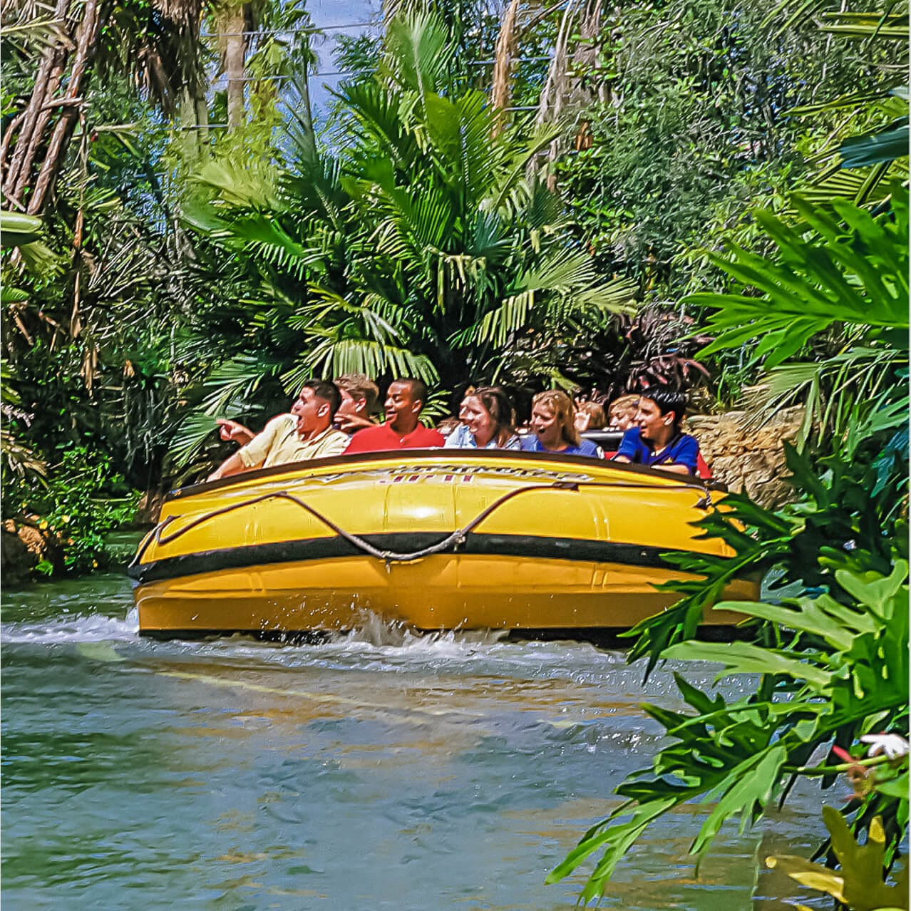 Tropical view of guests floating in their boat through a jungle scene on the Jurassic Park River Adventure water thrill ride at Universal Orlando.