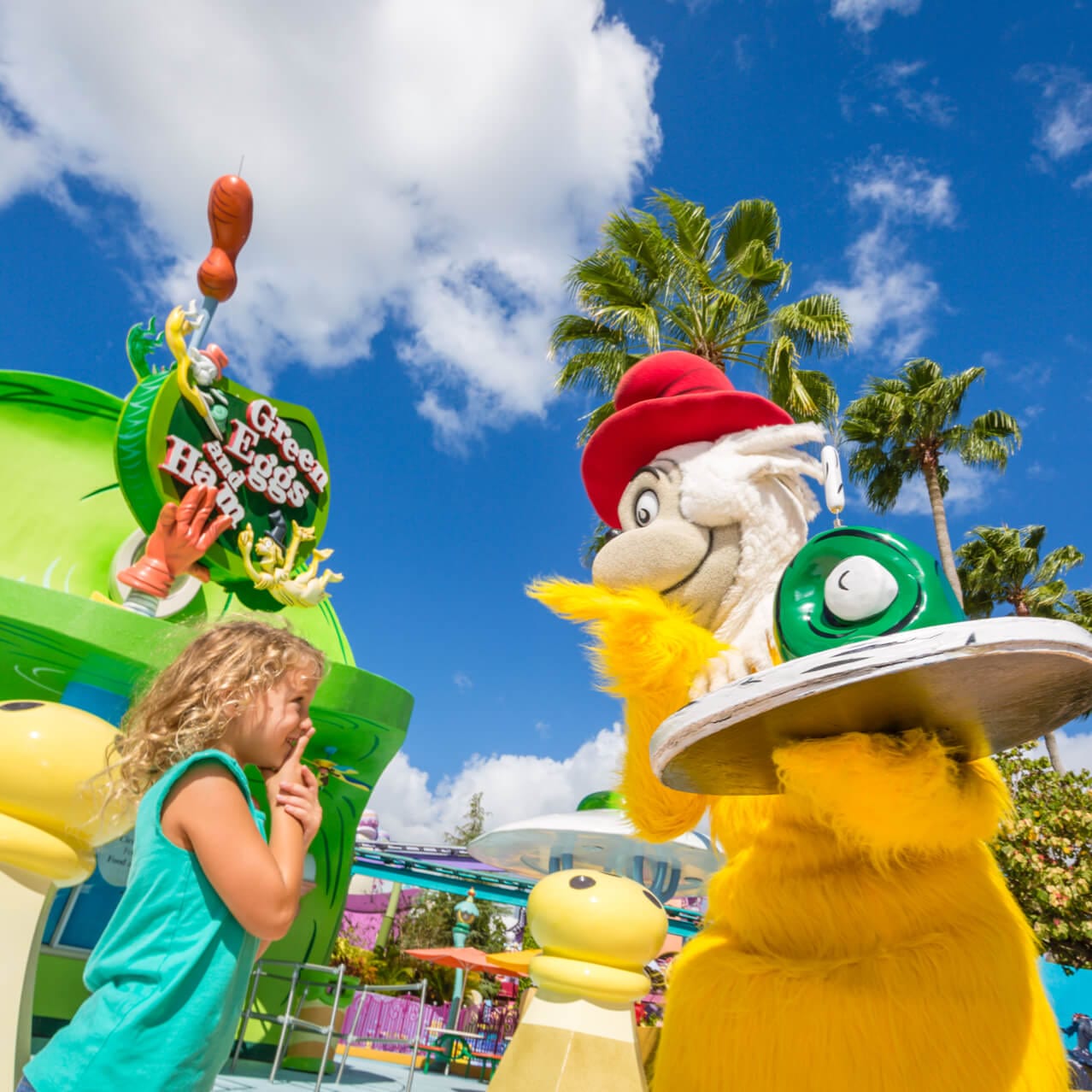 Dr. Seuss character Sam I Am holds a platter of green eggs and ham in front of a little girl inside Universal's Seuss Character Zone.