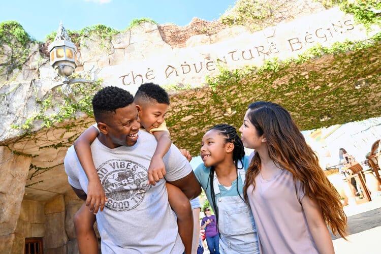 A happy family of four standing together in front of “The adventure begins” at Port of Entry inside Universal Islands of Adventure.
