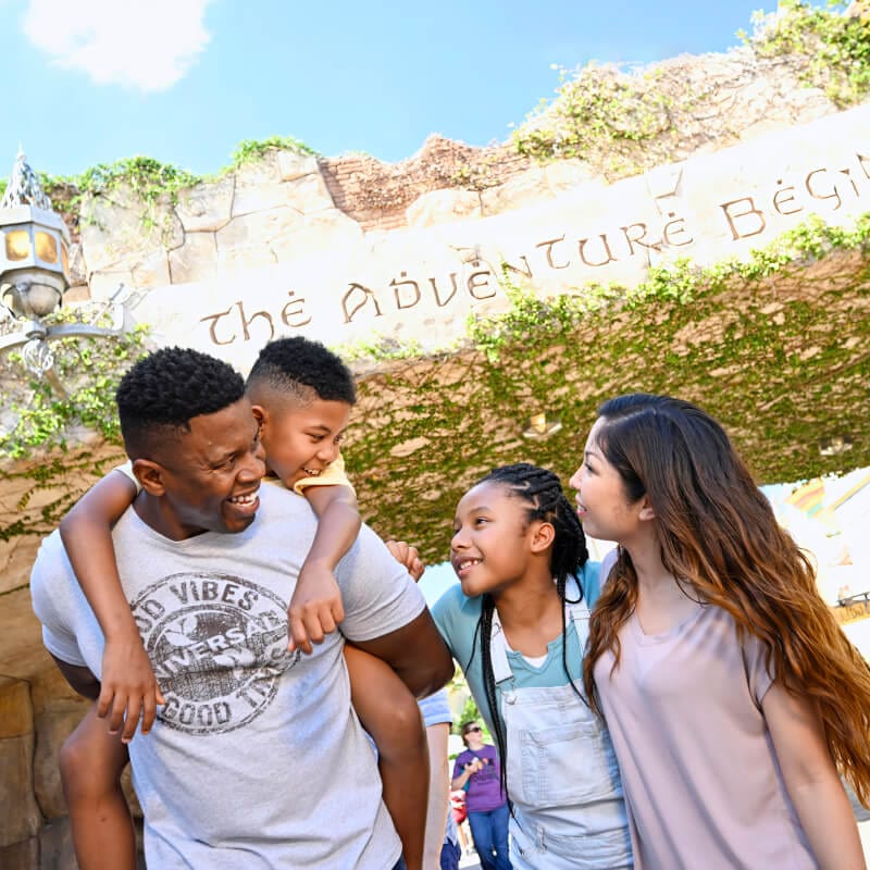 A happy family of four standing together in front of “The adventure begins” at Port of Entry inside Universal Islands of Adventure.