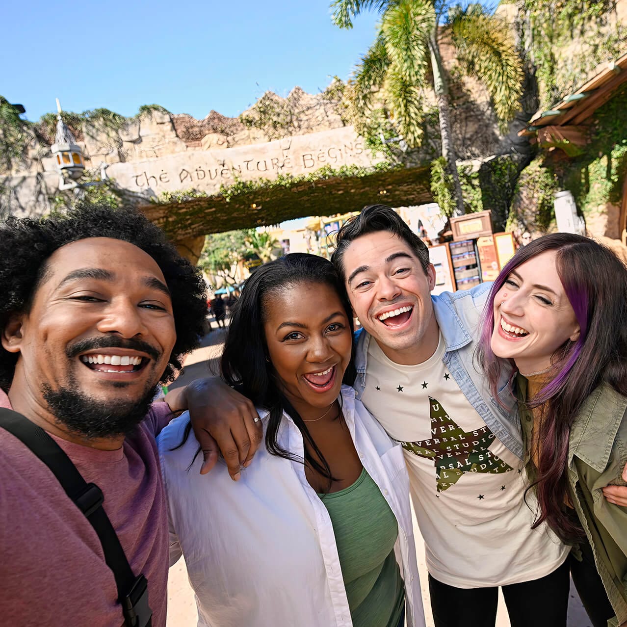 A group of friends happily pose together in front of “The Adventure Begins” at Port of Entry inside Universal Islands of Adventure.