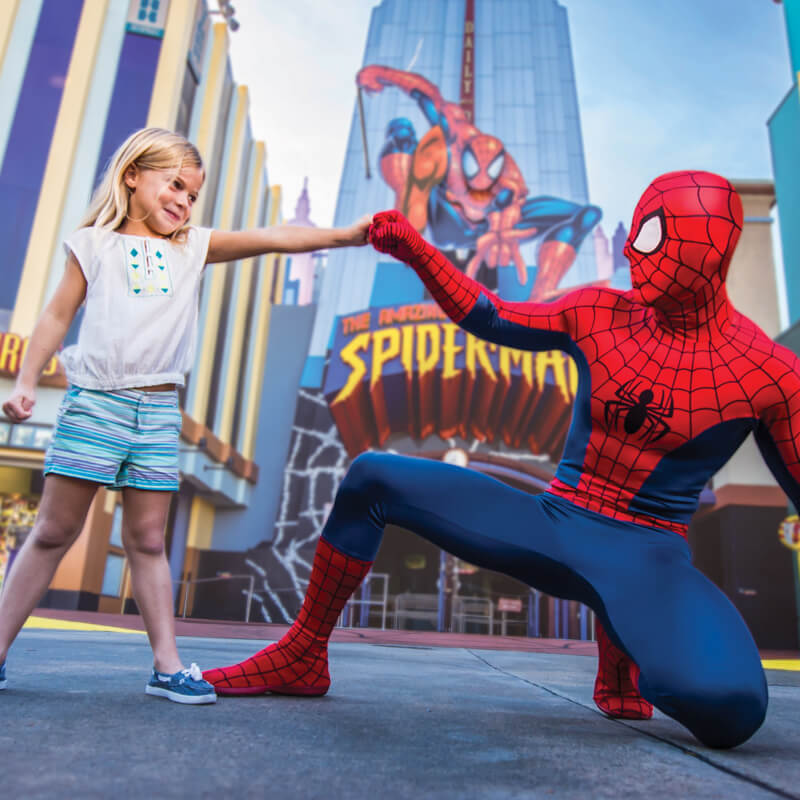 A girl fist bumps Spider-Man in front of the Spider-Man ride at Universal Islands of Adventure.
