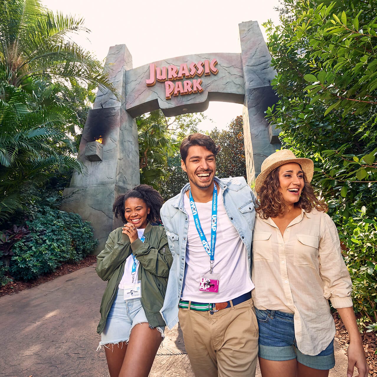 Three Passholder friends walking and smiling in front of the Jurassic Park archway in Universal Island s of Adventure.