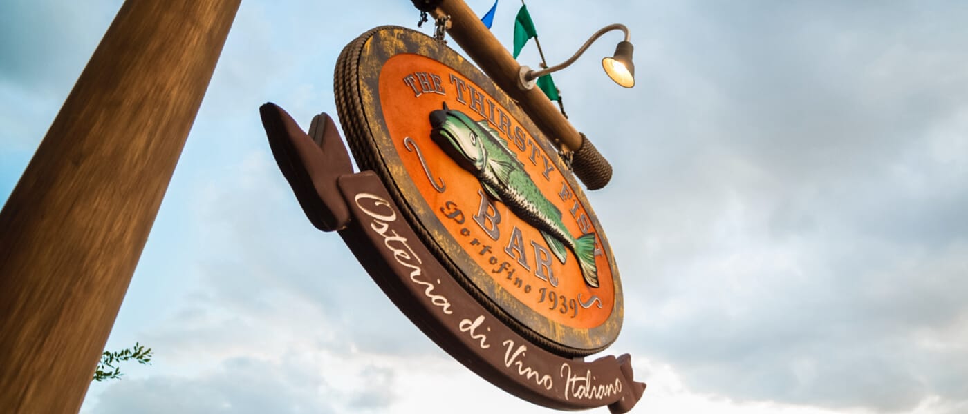 An orange sign is adorned with a fish character outside The Thirsty Fish, a casual waterfront bar at Loews Portofino Bay Hotel.