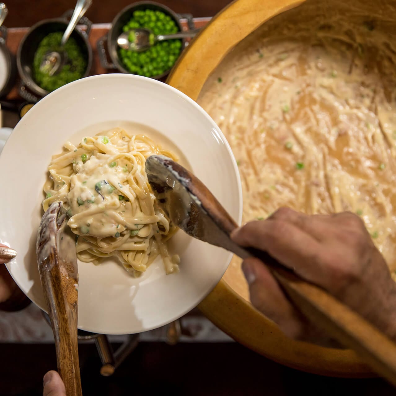 An overhead image of pasta being scooped form a large dish onto a serving plate at Mama Della's Ristorante at Universal Orlando Resort.