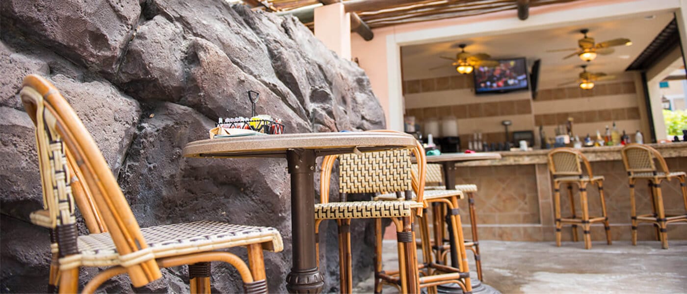 A cafe table with woven chairs beneath a flat screen TV inside the shaded dining area of Splendido Bar and Grill.