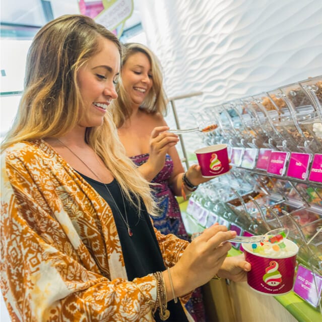 Two girls scoop sweet and savory toppings onto their cups of yogurt at Menchie's Frozen Yogurt.