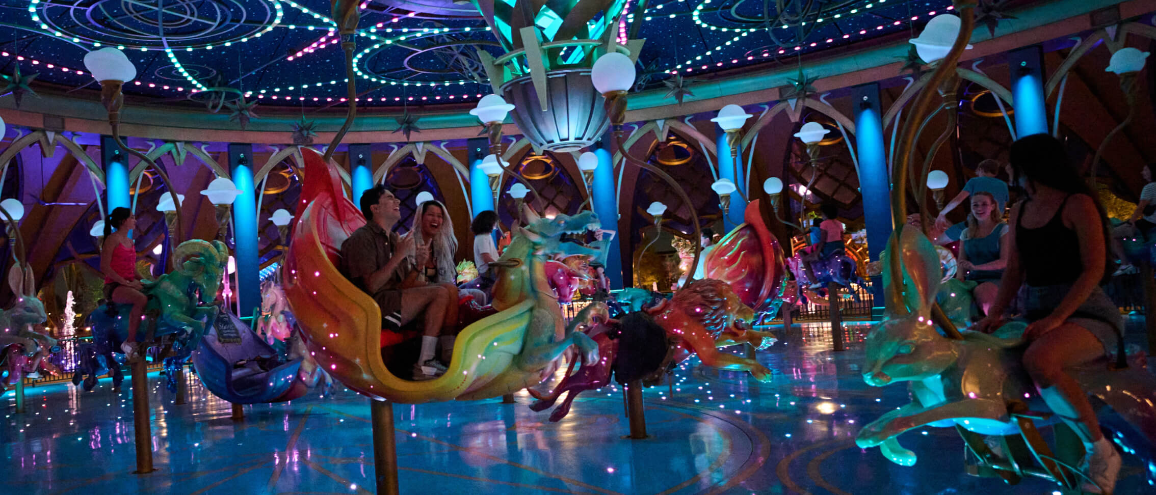 Excited Guests riding in colorful animal-shaped carousel vehicles under a ceiling of dazzling lights and starry fields.