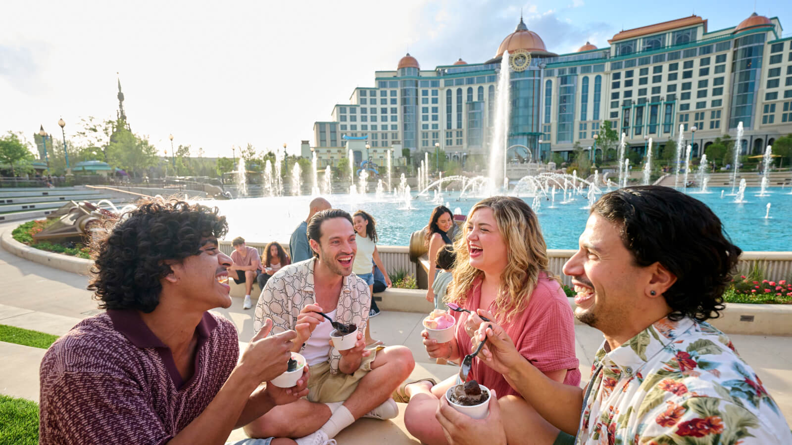Guests enjoy ice cream by the fountain in Celestial Park with Universal Helios Grand Hotel behind them.