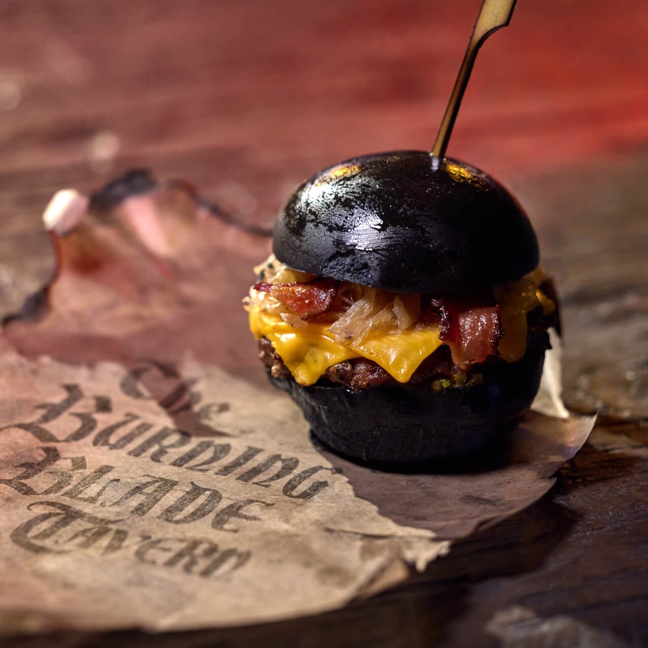 Burning Blade Burger, made of black Angus patty with American cheese, caramelized onions, jalapeño bacon on a black potato bun, served at The Burning Blade Tavern.