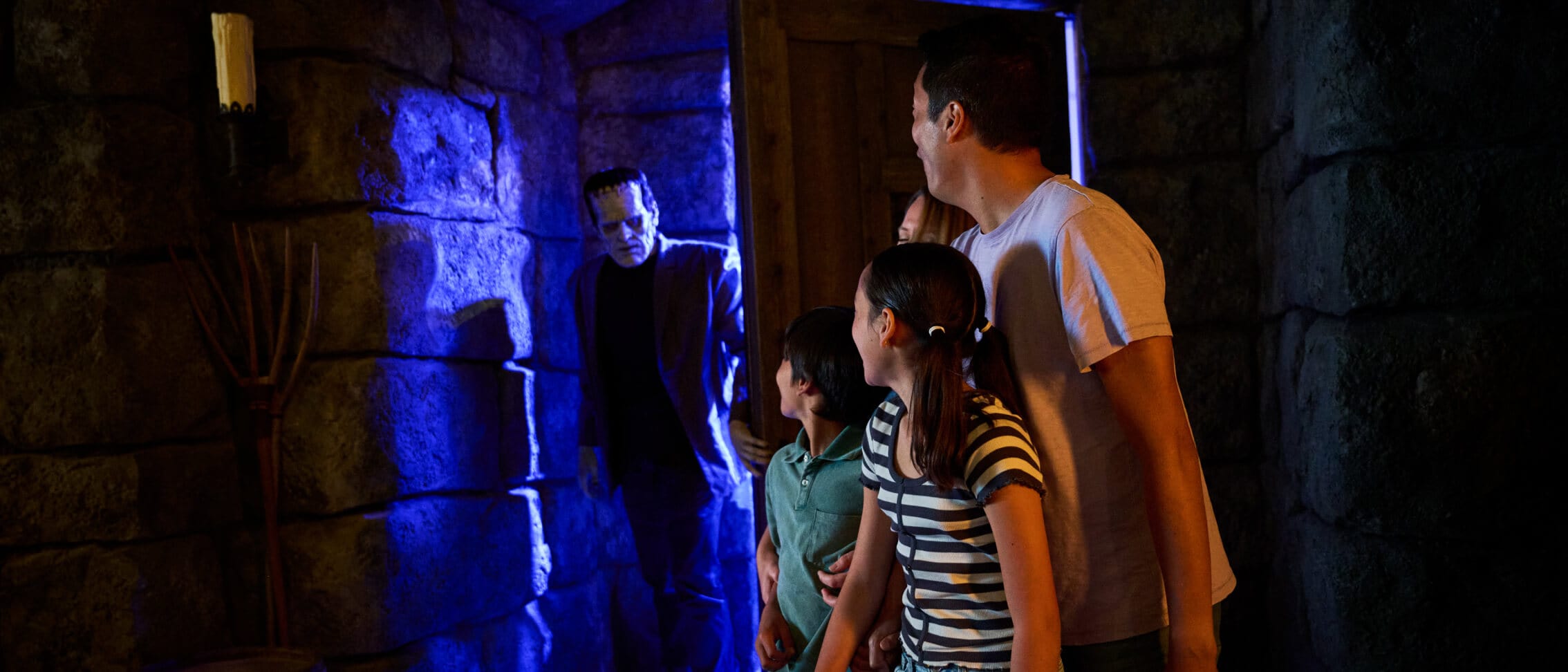 A young family looks back over their shoulder as Frankenstein's Monster walks through the door during a meet and greet in Dark Universe.