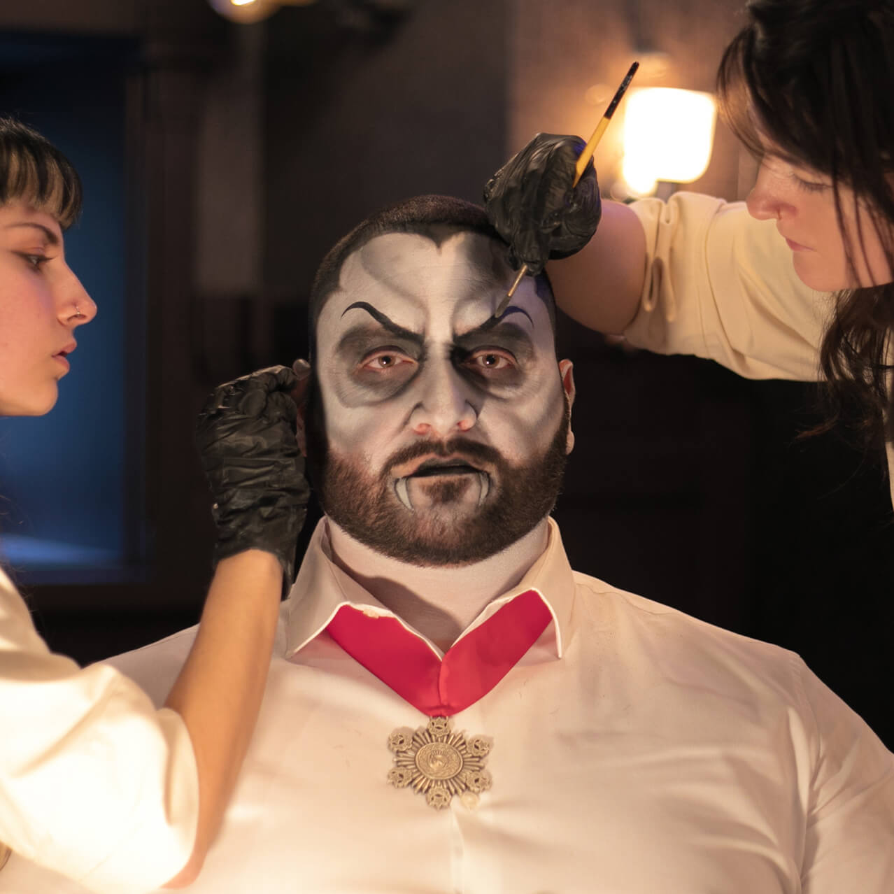 Two skilled artists of Darkmoor Monster Makeup Experience work on a customer's face makeup, transforming him into a vampire.