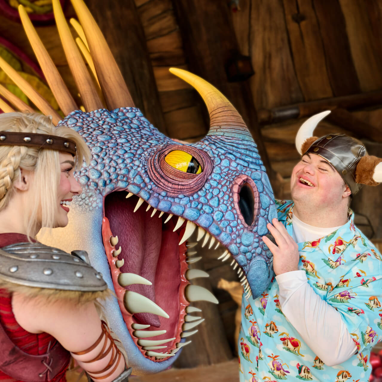 A smiling Guest in a horned helmet interacting with a blue dragon while a blonde Viking character looks on.