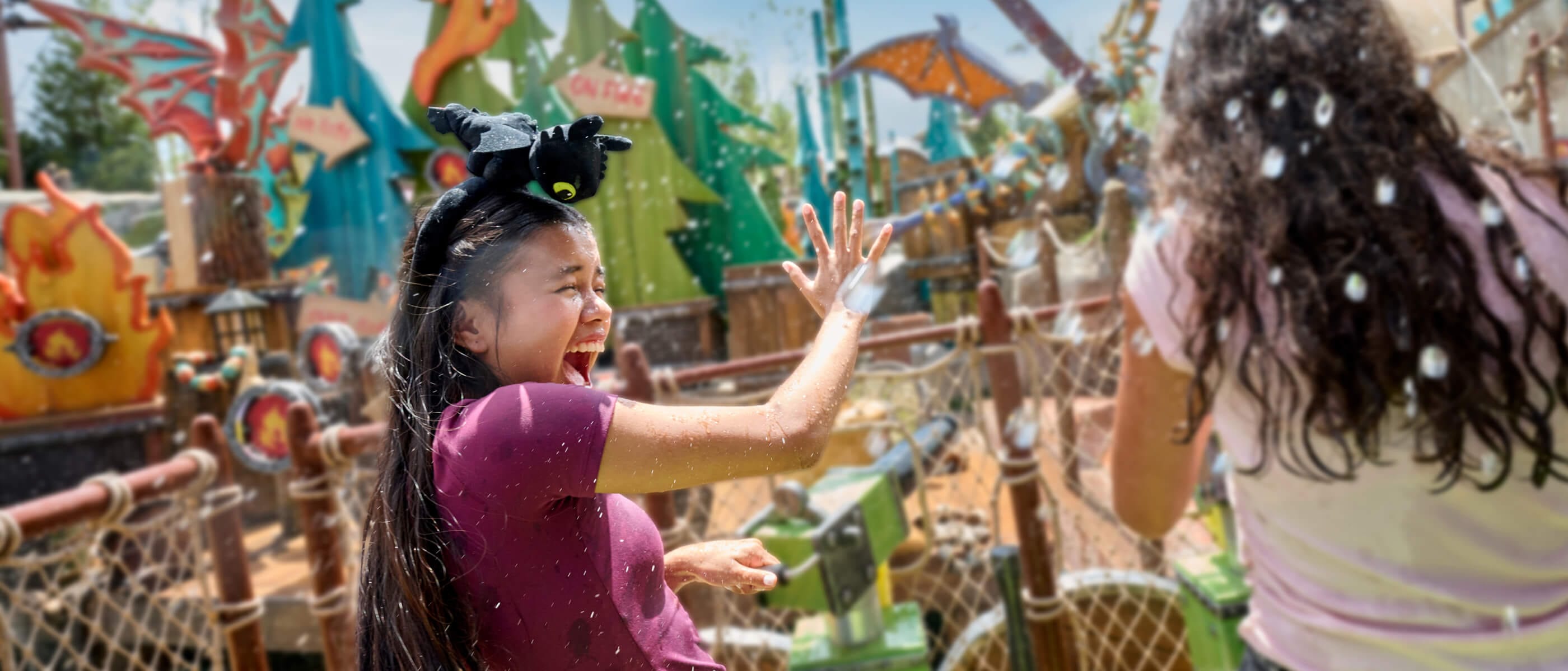 Young Guests holding green water shooters laughing as they get splashed, with fire- and tree-shaped cutouts in the distance