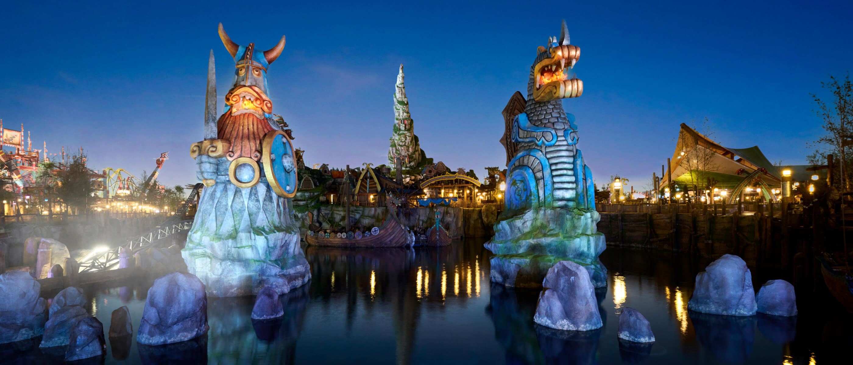 Illuminated Viking and dragon statues guard a waterway, with a glowing Mead Hall in the background.