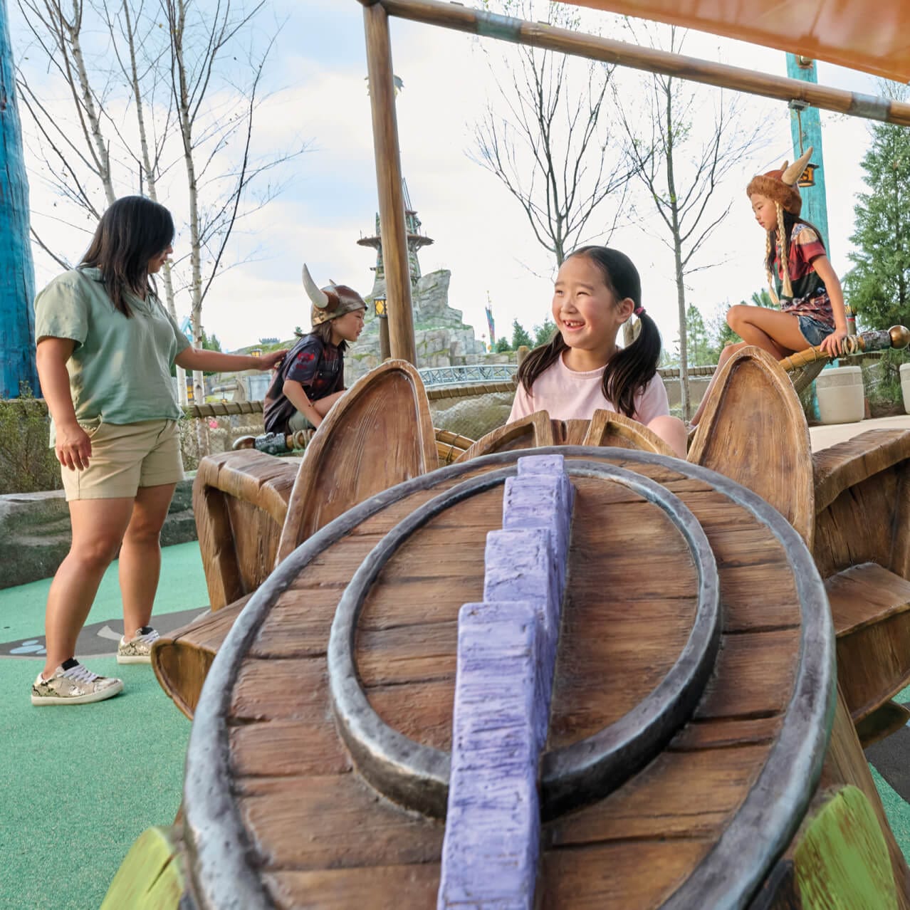 A young girl smiles bright as she plays on the dragon-themed playground at the Viking Training Camp in How to Train Your Dragon – Isle of Berk
