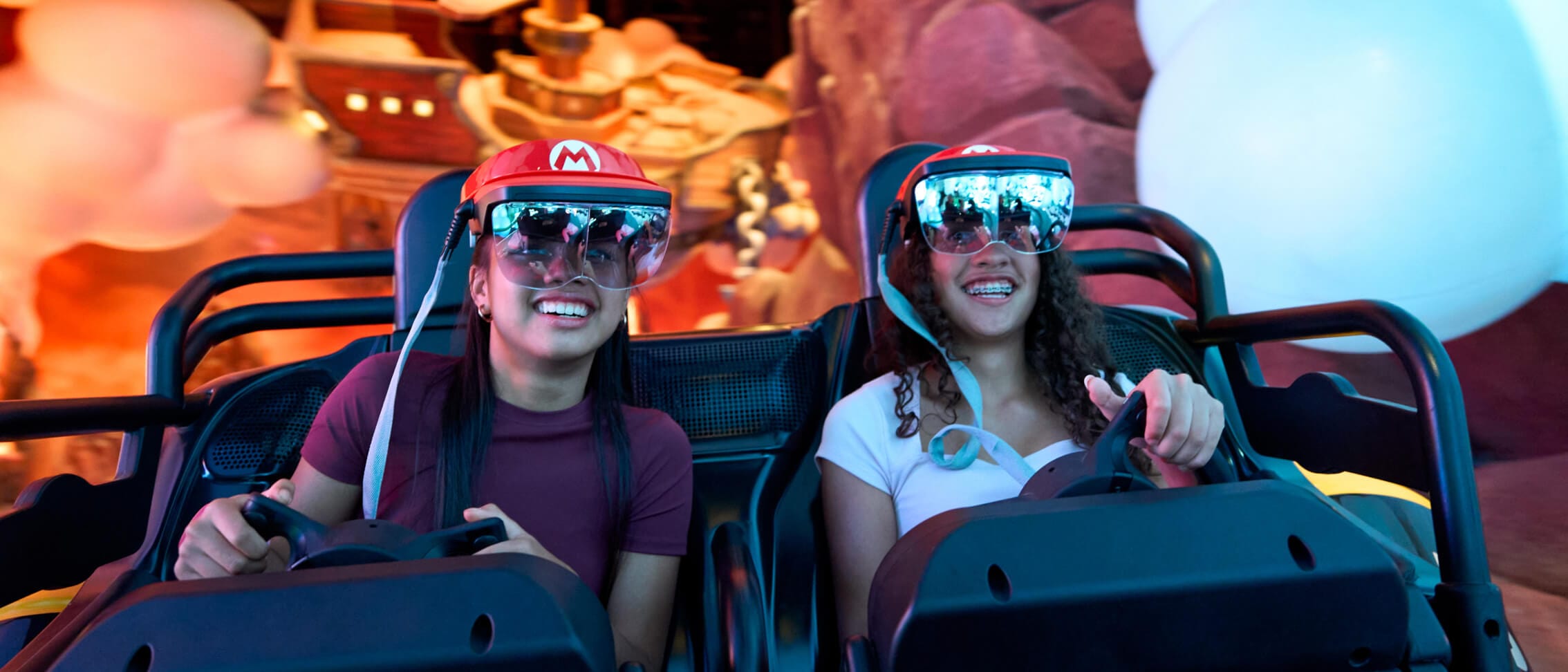 Two girls smile as they steer through Mario Kart: Bowser's Challenge in SUPER NINTENDO WORLD™ at Universal Epic Universe.