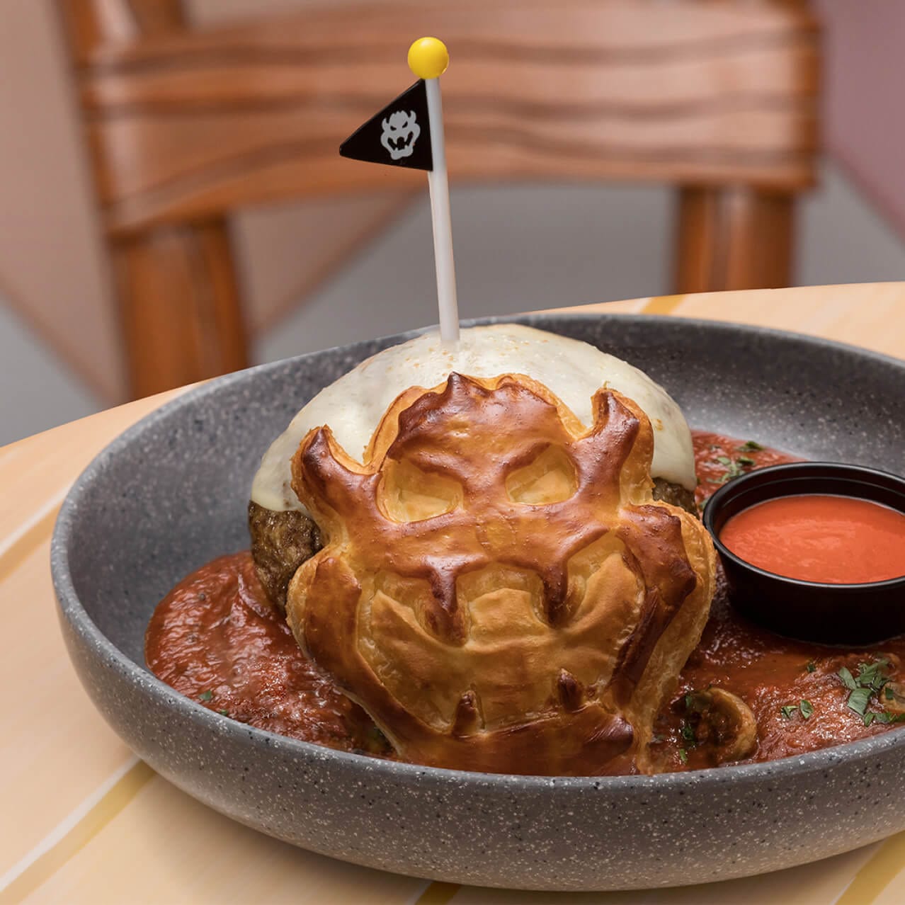 Plate with a giant meatball topped with mozzarella cheese, a Bowser-shaped puff pastry and pasta sauce, available at Toadstool Cafe.