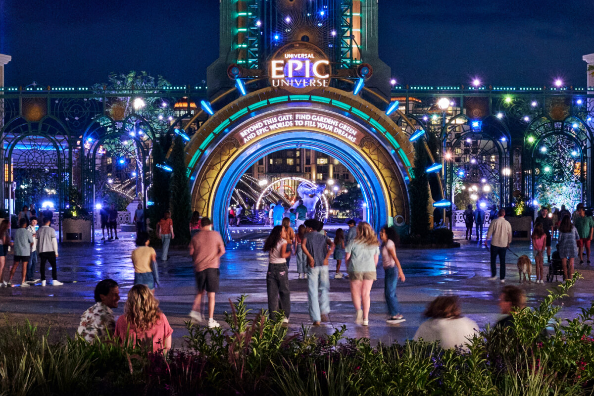 Guests walk toward the brightly lit main entrance of Universal Epic Universe, with Chronos rising overhead against the night sky.