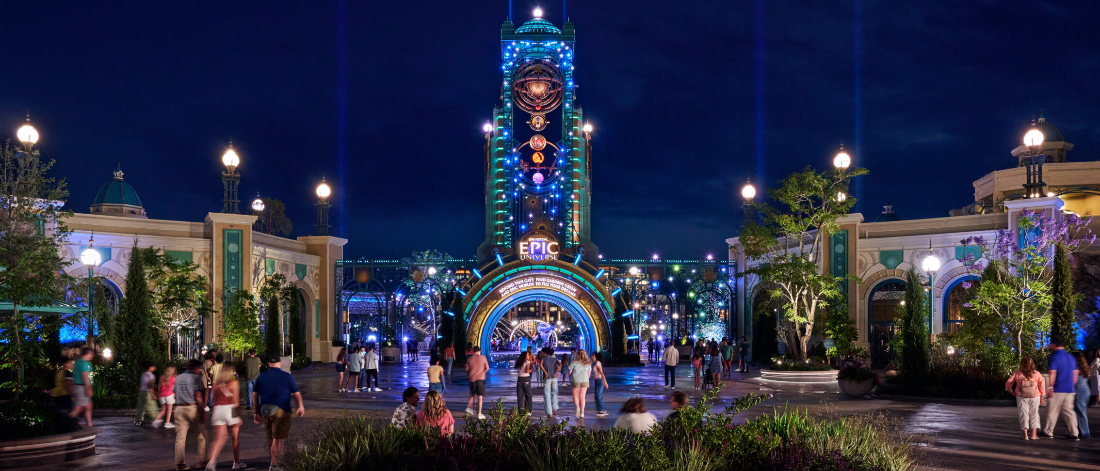 Guests walk toward the brightly lit main entrance of Universal Epic Universe, with Chronos rising overhead against the night sky.
