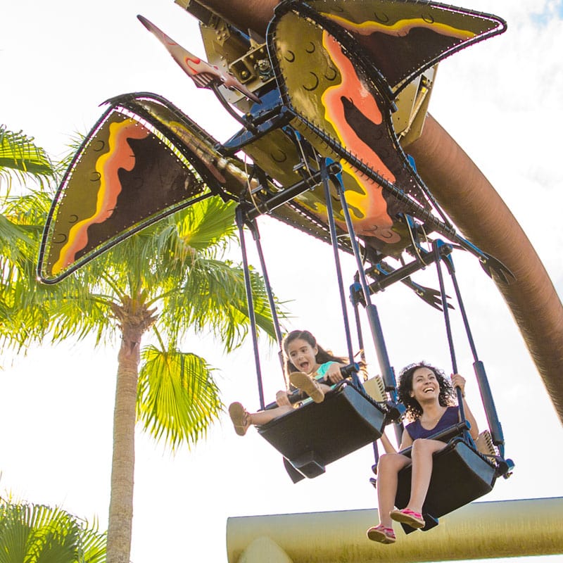 A girl and mother soar through the air on the Pteranodon Flyers children's ride.