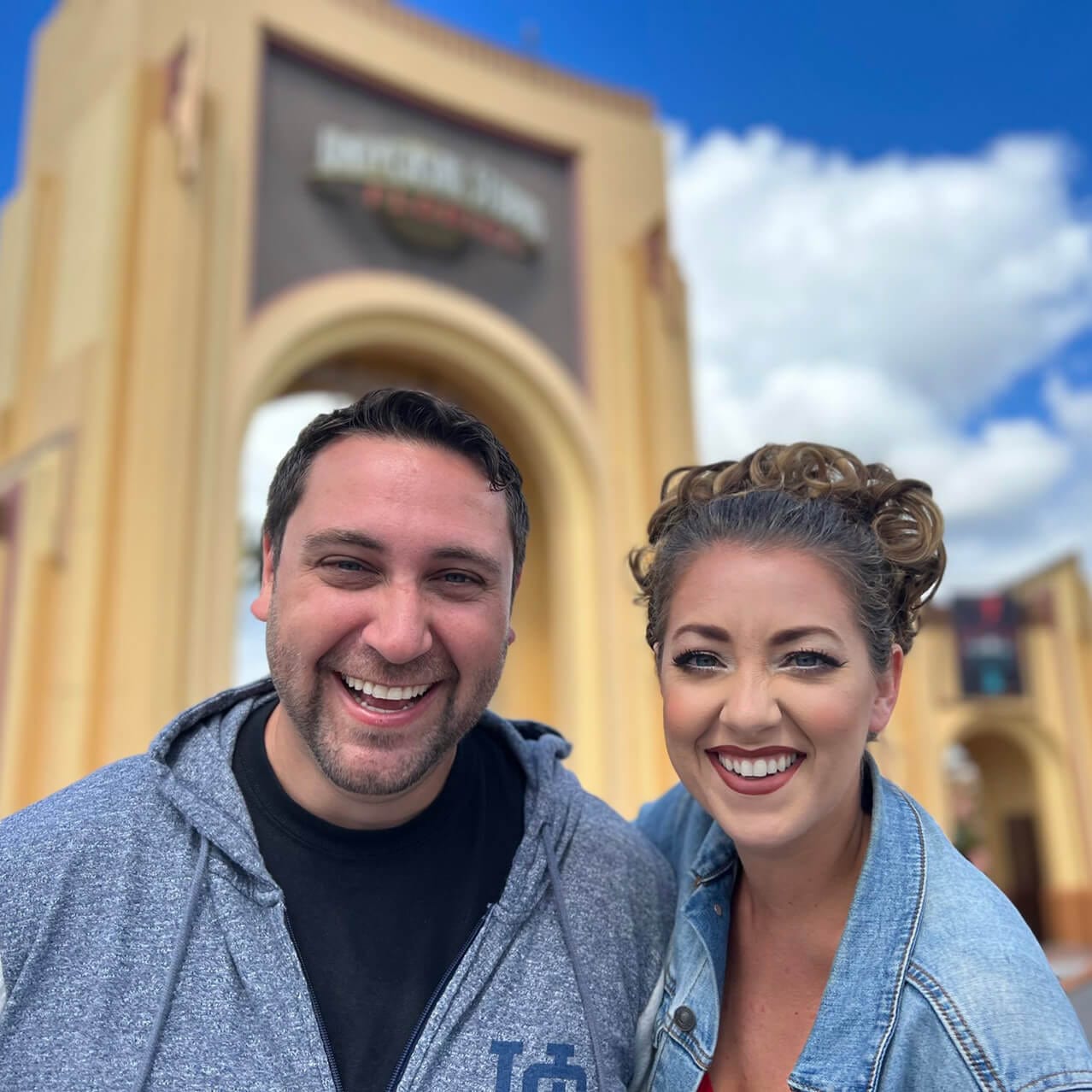 The hosts of the Discover Universal Podcast smiling as they pose in front of the arched entryway at the front of Universal Studios Florida.