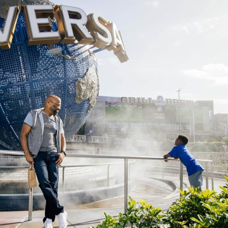 A smiling father watching his son gaze through the mist at the iconic globe outside the Universal Studios Florida entrance.