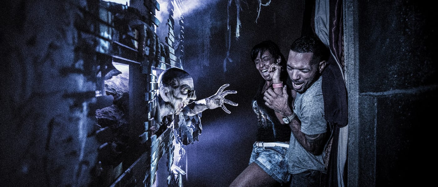 A couple screams in terror as a creature lunges at them in a Halloween Horror Nights haunted house.