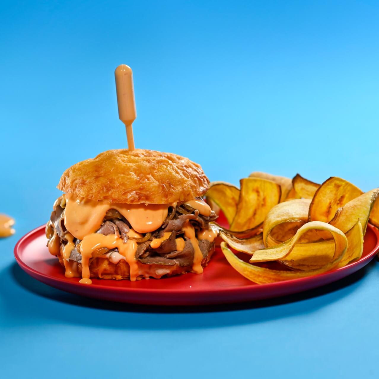 Steak & "Cheese Ray" Sandwich on a blue background with cheese sauce around the plate.