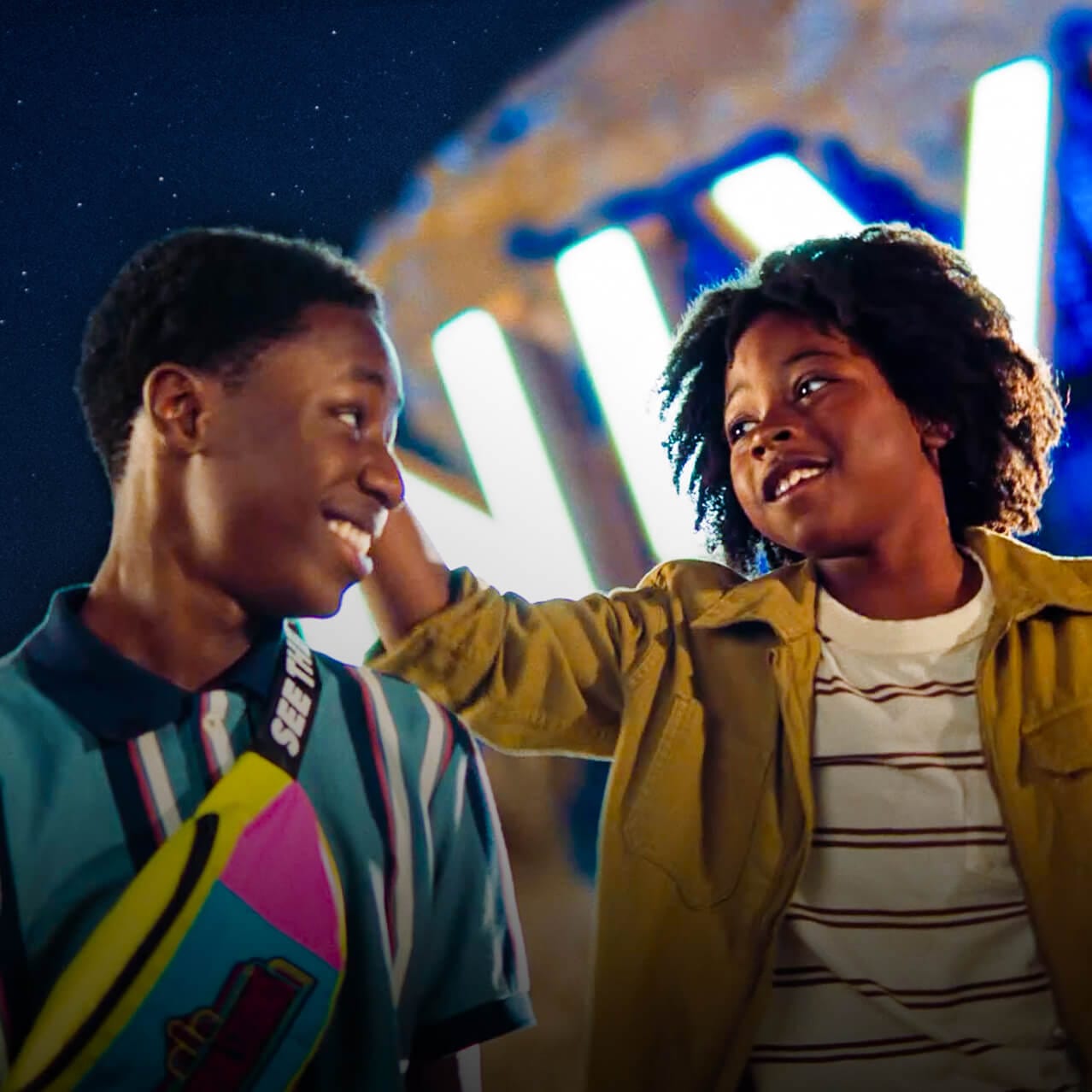 A young Guest and his older brother smiling at each other as the iconic Universal globe glows behind them.