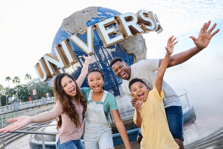An excited family of four posing with the Universal Globe in front of the entrance to Universal Studios Florida.