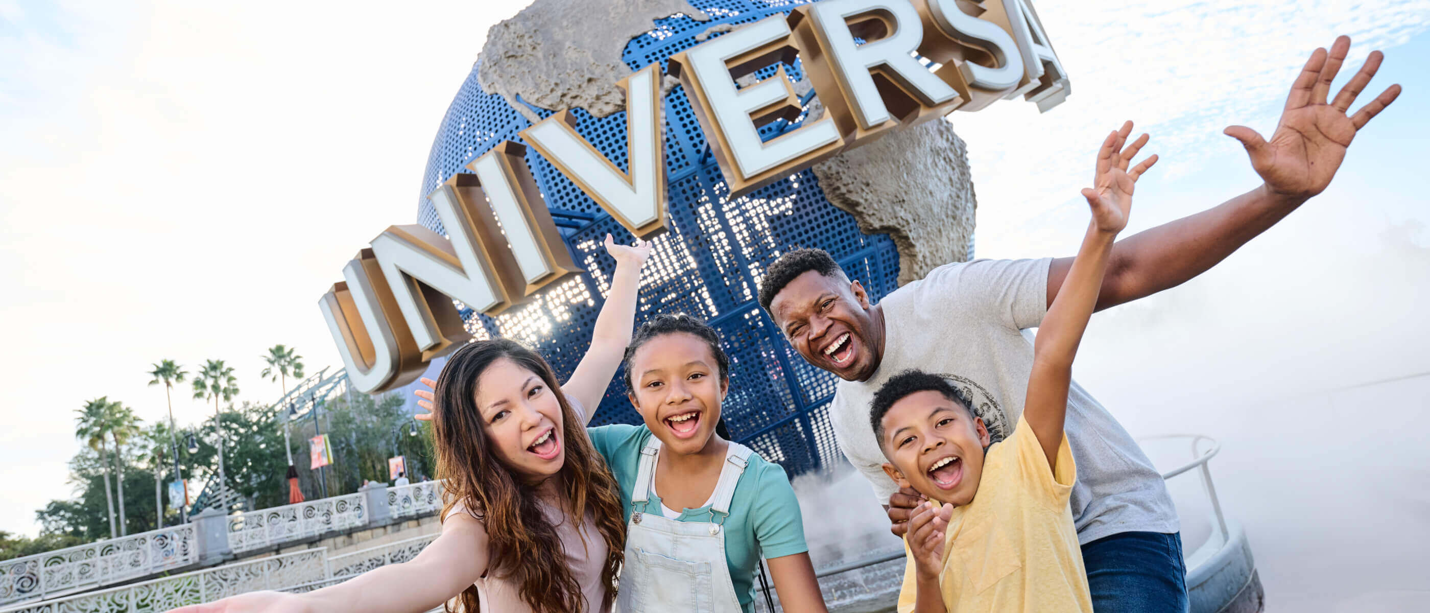 An excited family of four pose with the Universal Globe in front of the entrance to Universal Studios Florida.