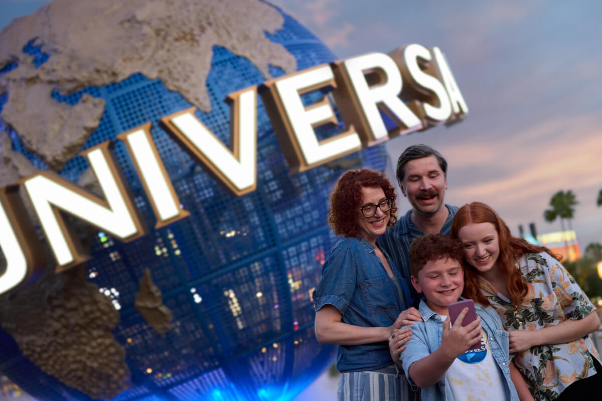 A family of four smiling excitedly as they pose for a selfie together in front of the iconic Universal globe.
