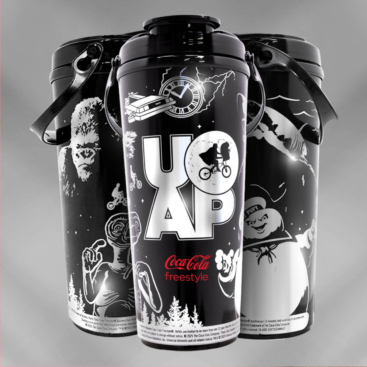 Three black and silver Coca-Cola Freestyle Cups featuring E.T., Jaws, Back to the Future, Ghostbusters and King Kong.