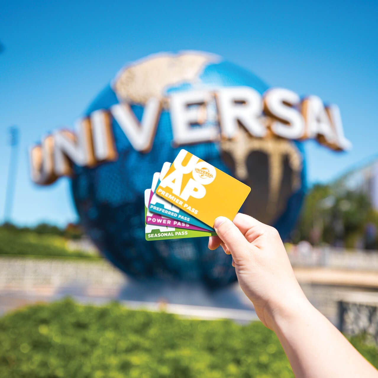A hand holding four kinds of Universal Orlando Annual pass in front of the Universal globe.
