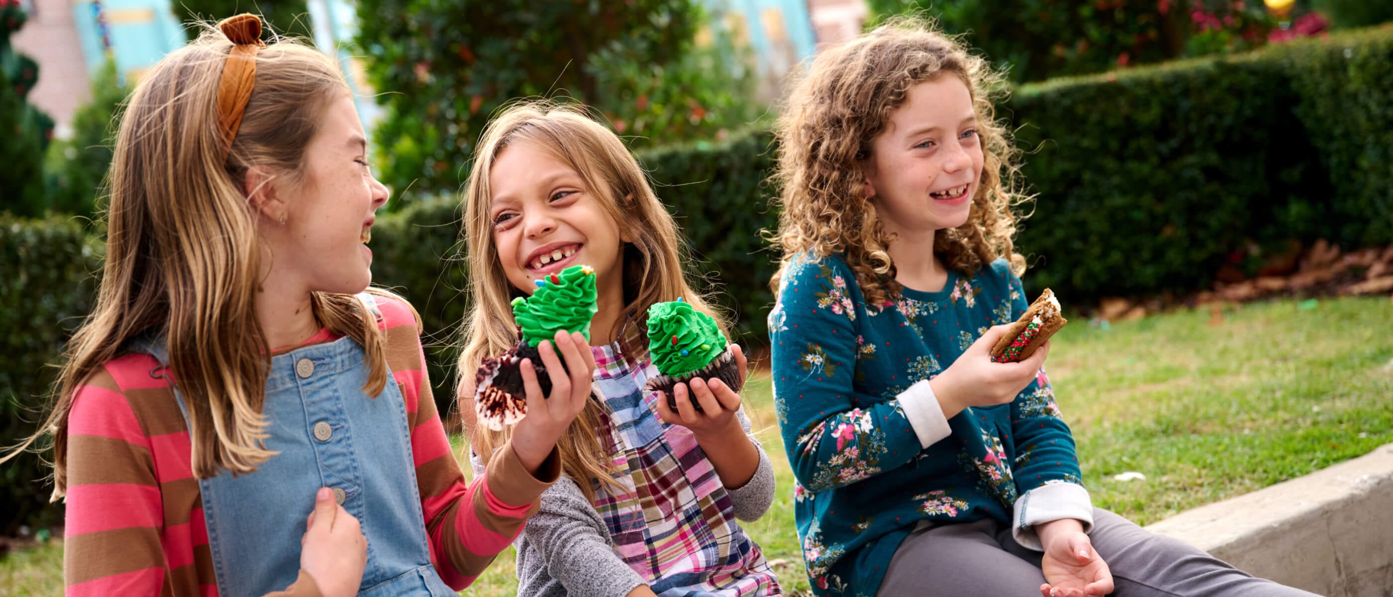 Three girls enjoying Christmas decorated cupcakes and cookie sandwiches as they sit on the curb in Central Park at Universal Studios Florida.