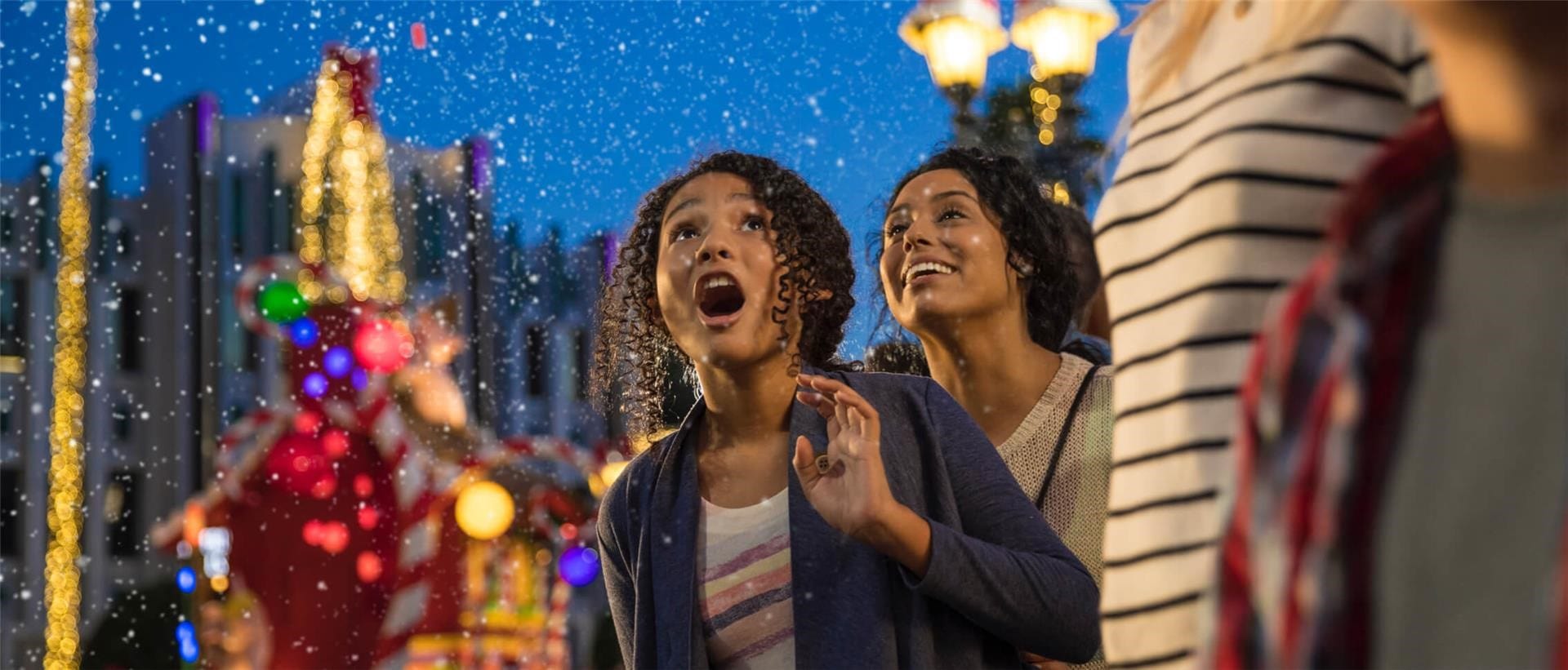 A girl and her mother look up in wonder at snow falling during Universal Orlando's holiday parade.