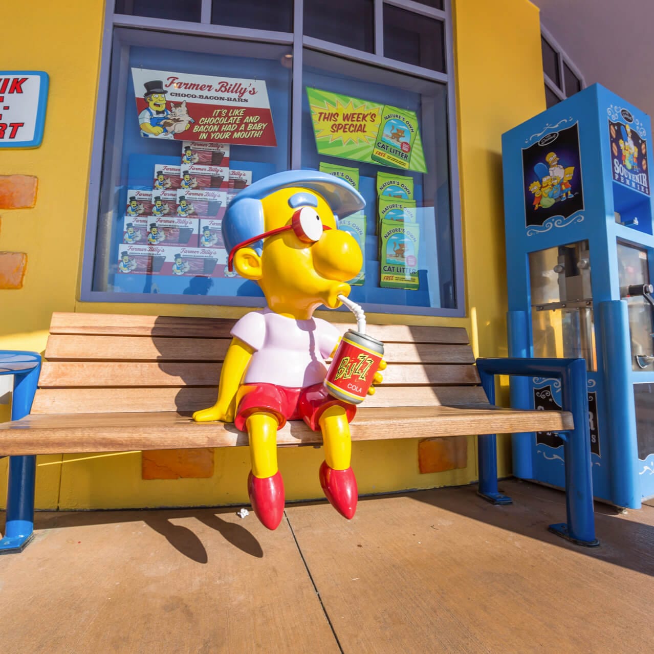 A statue of the Simpsons character Milhouse Mussolini Van Houten sitting on a bench outside of Kwik E Mart in the Springfield area of Universal Studios Orlando.