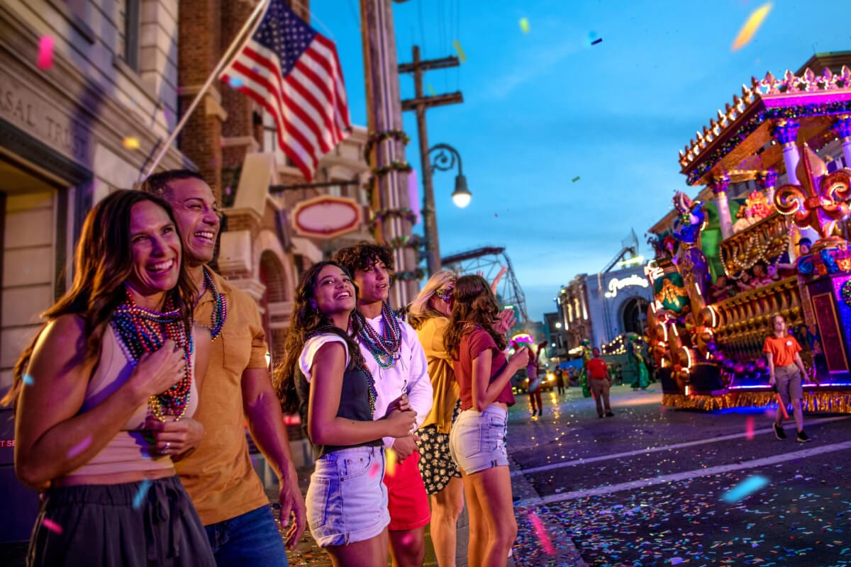 A group of guests on the side of the street cheer on the parade floats as they pass by at Universal Mardi Gras: International Flavors of Carnival.
