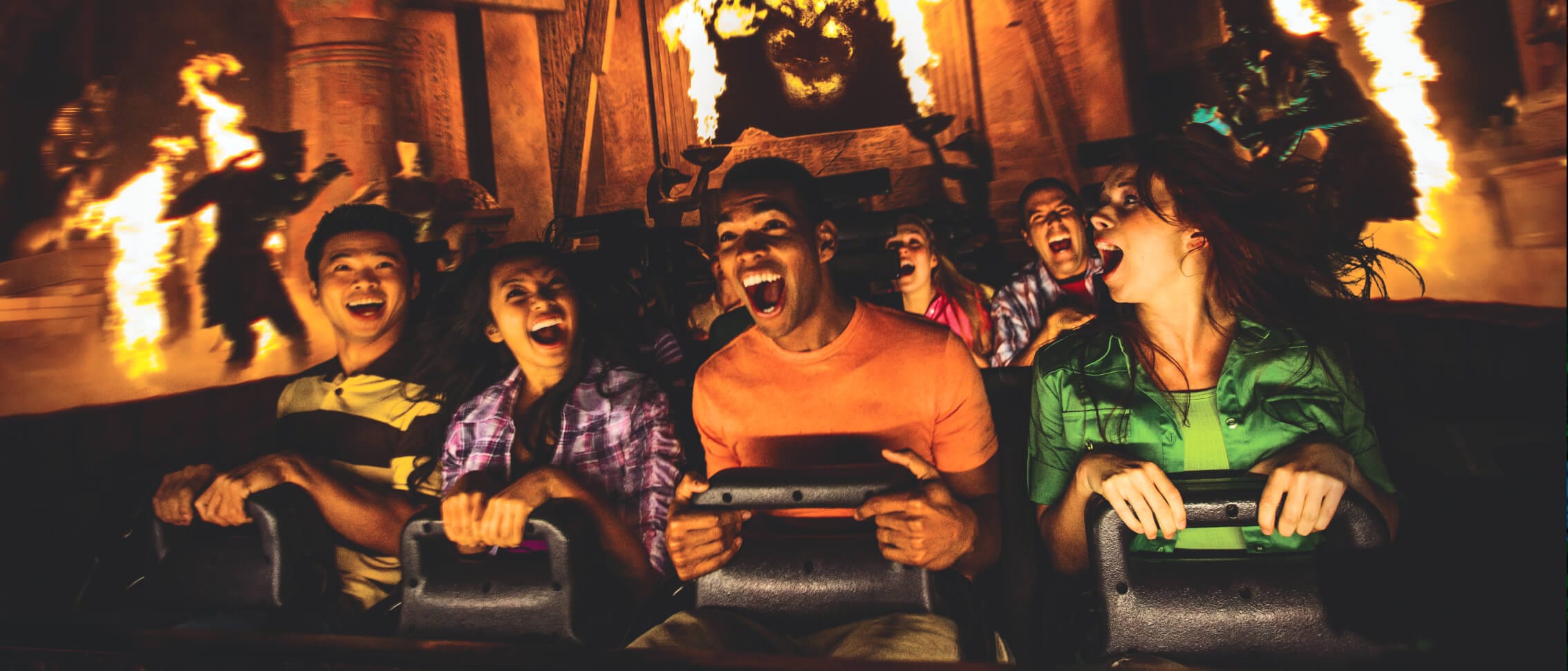 Friends holding on and screaming with laughter as they ride past mummified figures and bursts of flame on Revenge of the Mummy.